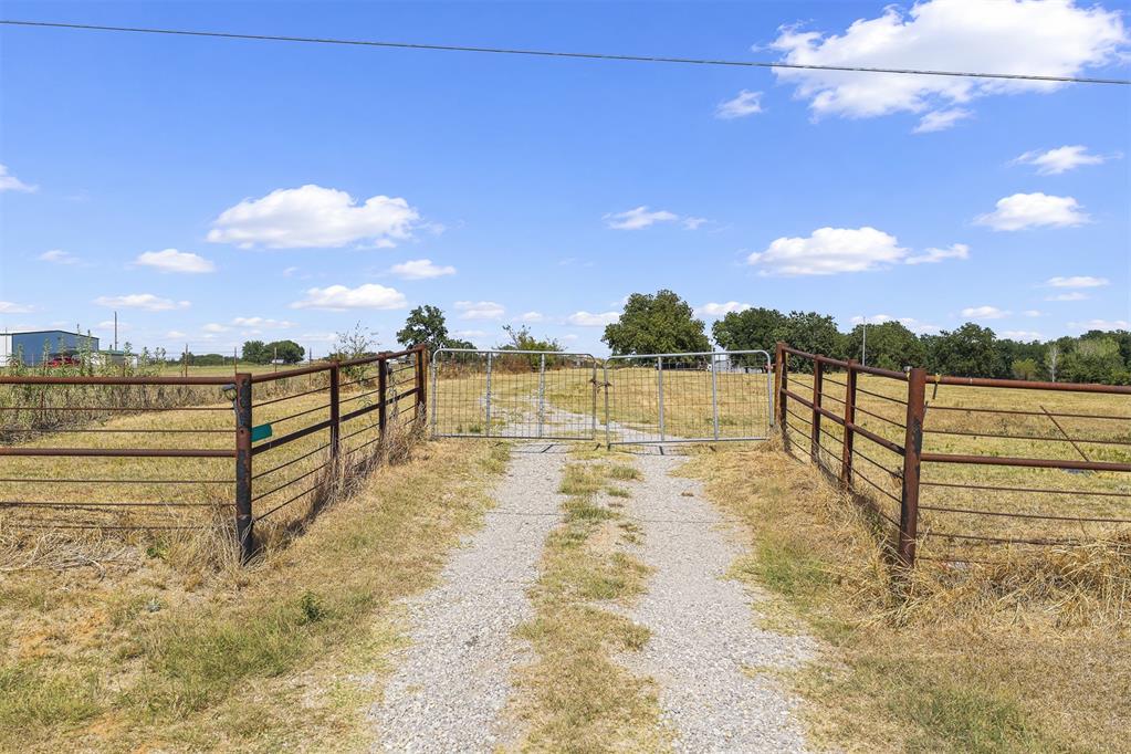 Gated gravel entrance to open acreage bordered by metal fencing.