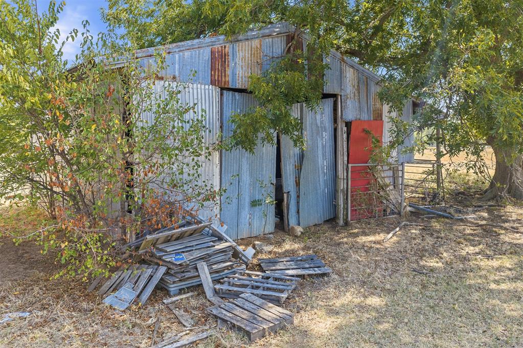 Weathered corrugated-metal outbuilding with open doors and discarded wooden pallets in front.