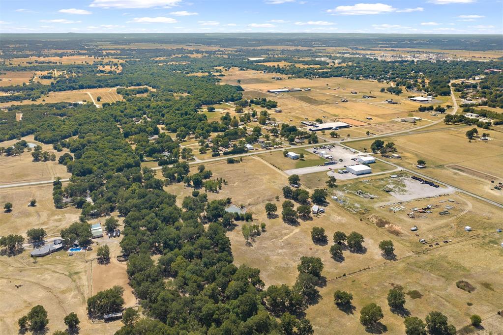 Aerial view of rural acreage with open fields, tree clusters, scattered buildings, and intersecting roads.