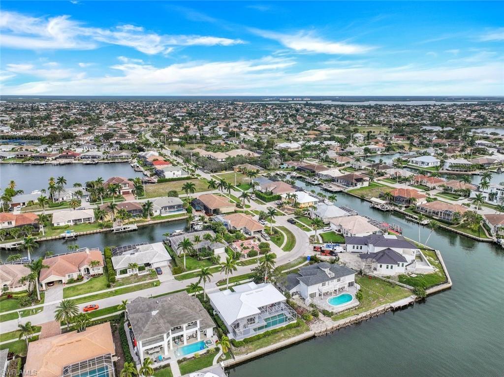 Aerial view of waterfront homes along canals, with docks, pools, and palm-lined streets.