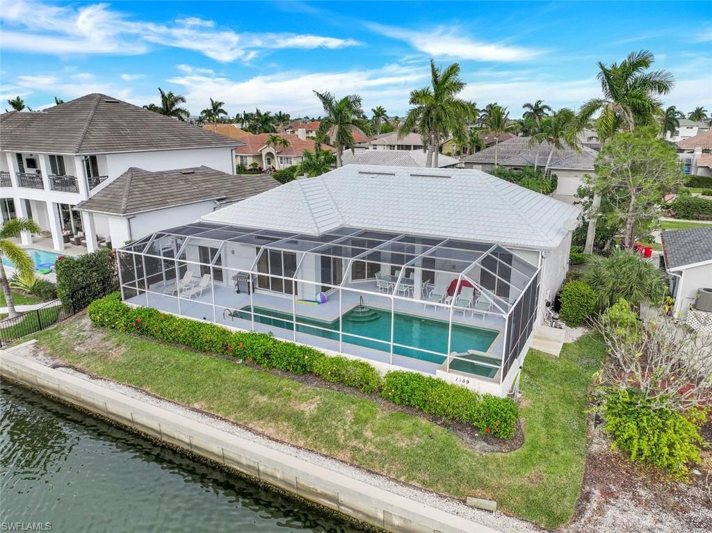 Aerial view of a canal-front home with a screened pool enclosure and palm-lined landscaping.