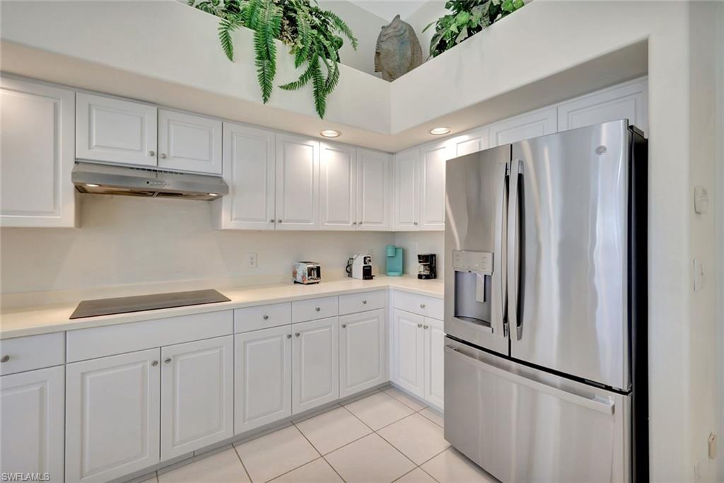 White kitchen with paneled cabinetry, stainless steel refrigerator, and tiled floor.
