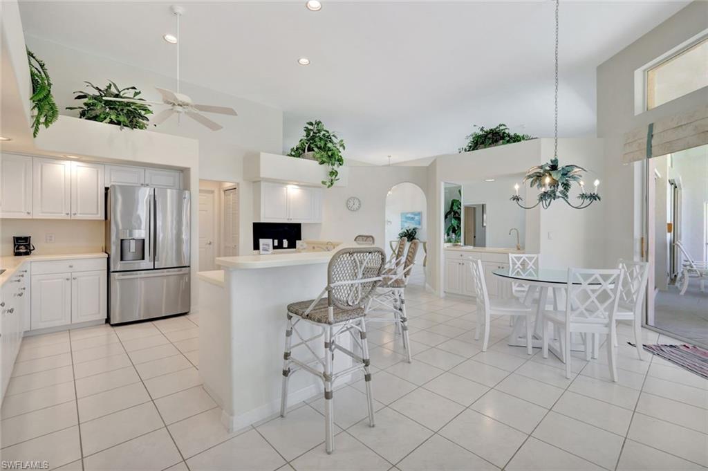 Open kitchen and dining area with a white island, stainless steel refrigerator, and glass dining table.