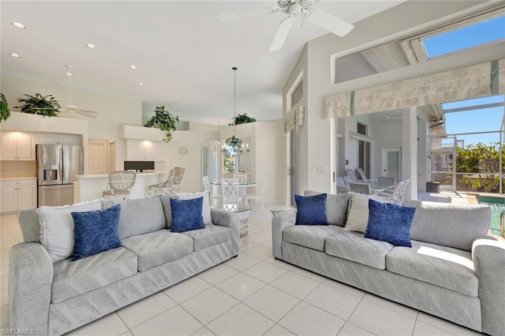 Living room with gray sofas and blue pillows, opening to the kitchen and a poolside lanai.