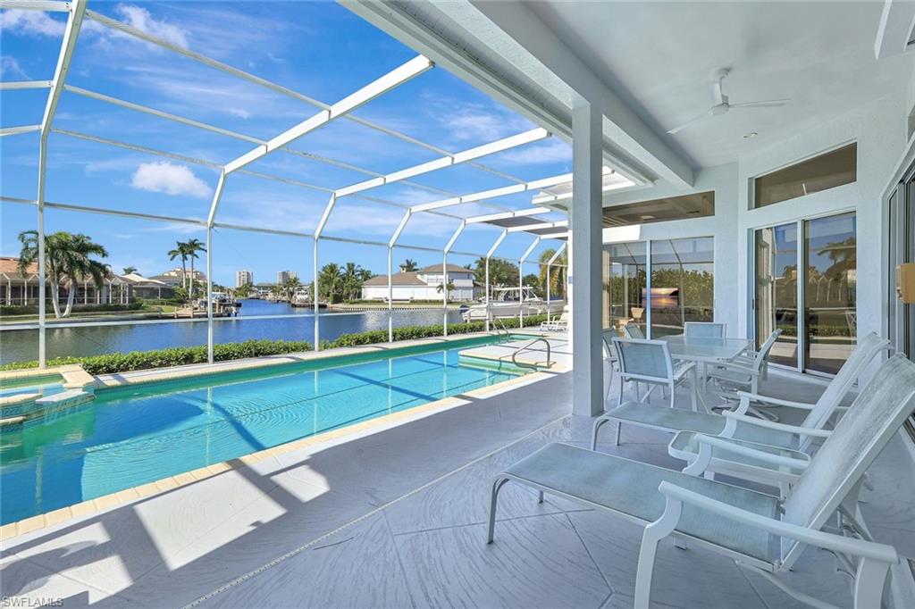 Covered patio with lounge chairs overlooks a pool and canal.