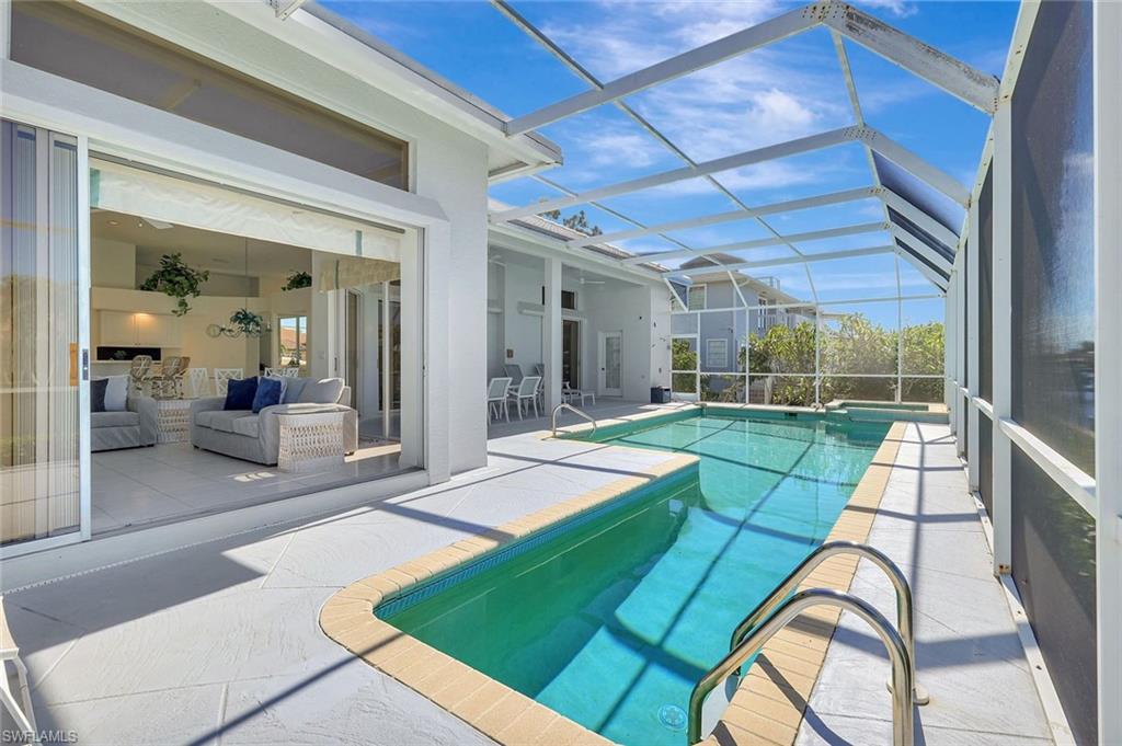 Screened swimming pool beside a furnished lanai and open sliding doors to the living room.