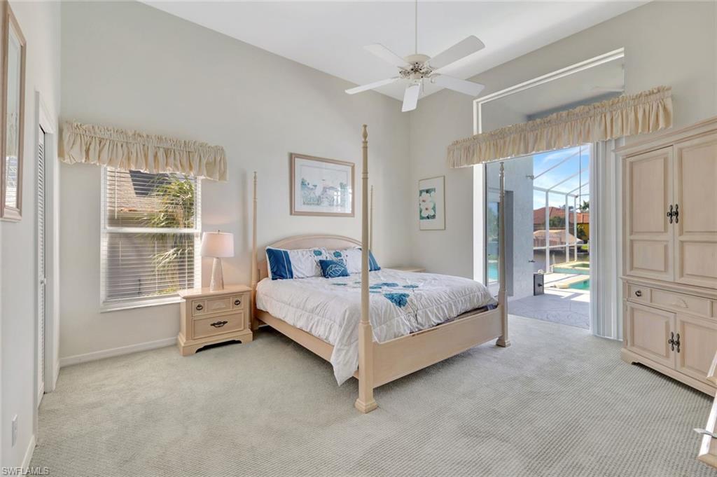 Bedroom with a cream four-poster bed and French doors overlooking a pool.