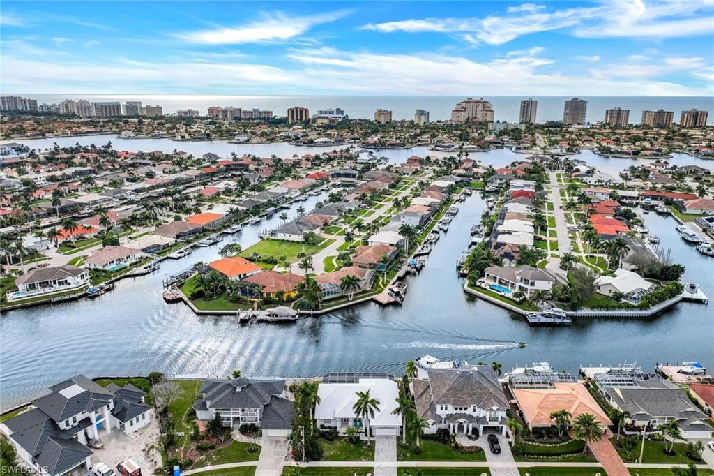 Aerial view of canal-front homes with docks and boats, backed by a distant coastal skyline.