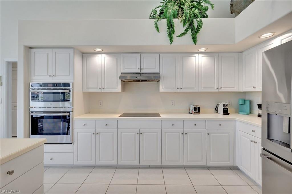 White kitchen with shaker cabinets, stainless steel double ovens, and a hanging fern.