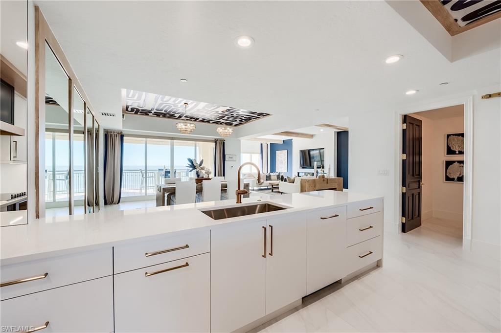 Modern white kitchen with a large island opening to living and dining areas with an ocean view.