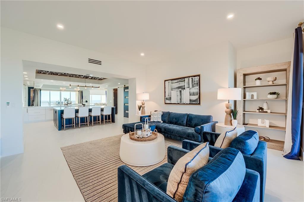 Living room with blue sofas, a round coffee table, and an open kitchen overlooking water.