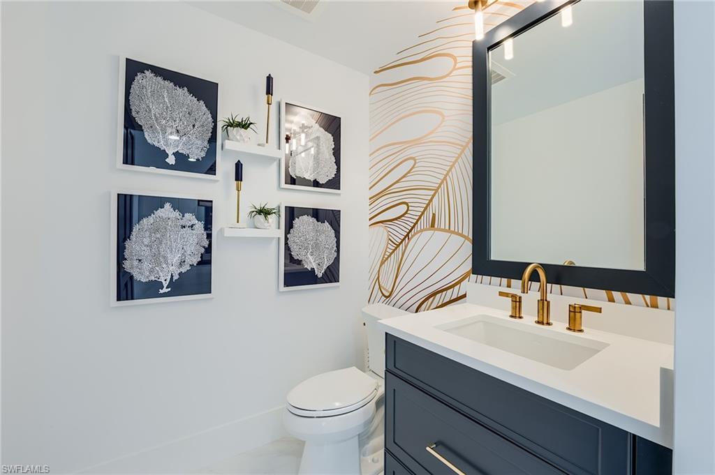 Bathroom with a navy vanity, brass fixtures, gold line-art wallpaper, and framed coral prints.