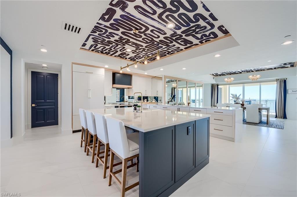 Contemporary condo kitchen with a dark blue island, white stools, and water views.