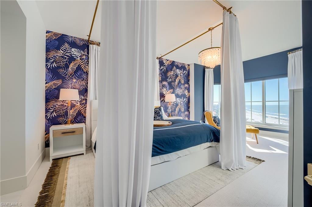 Bedroom with a white canopy bed, tropical accent wall, and ocean views through large windows.