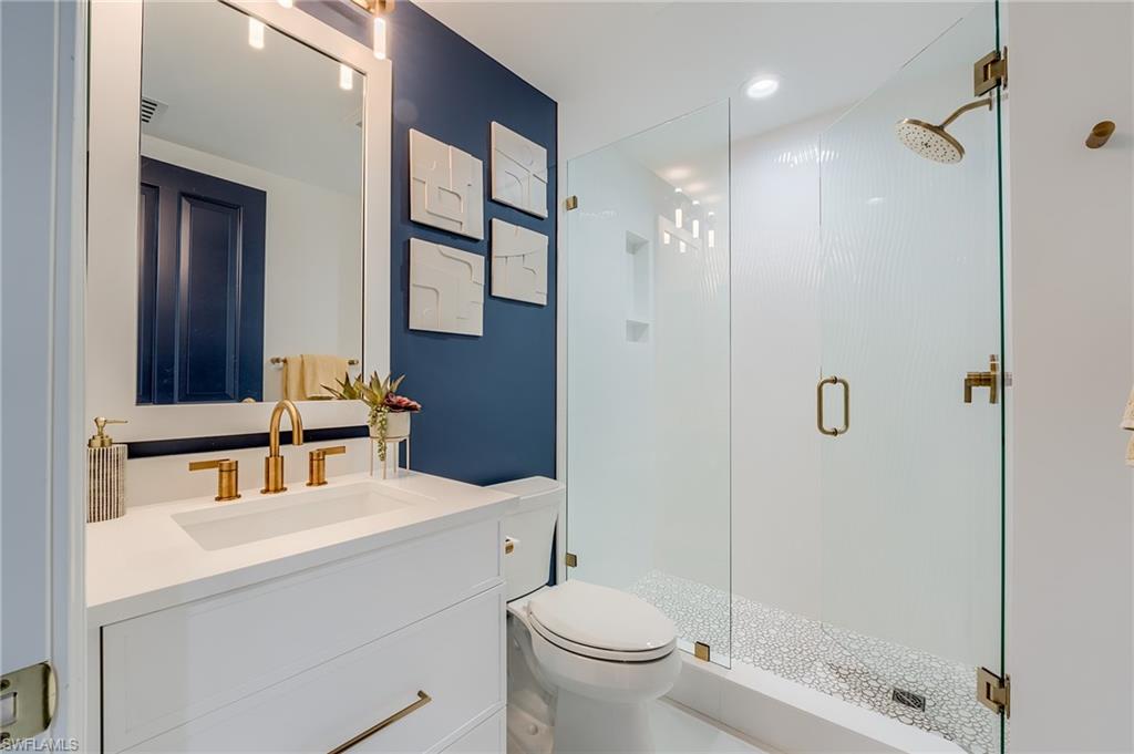 Modern bathroom with a white vanity, gold fixtures, and glass-enclosed pebble-floor shower.