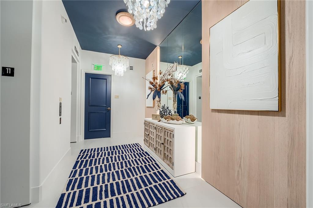 Condominium foyer with navy entry door, patterned runner, mirrored console, and crystal pendant lights.