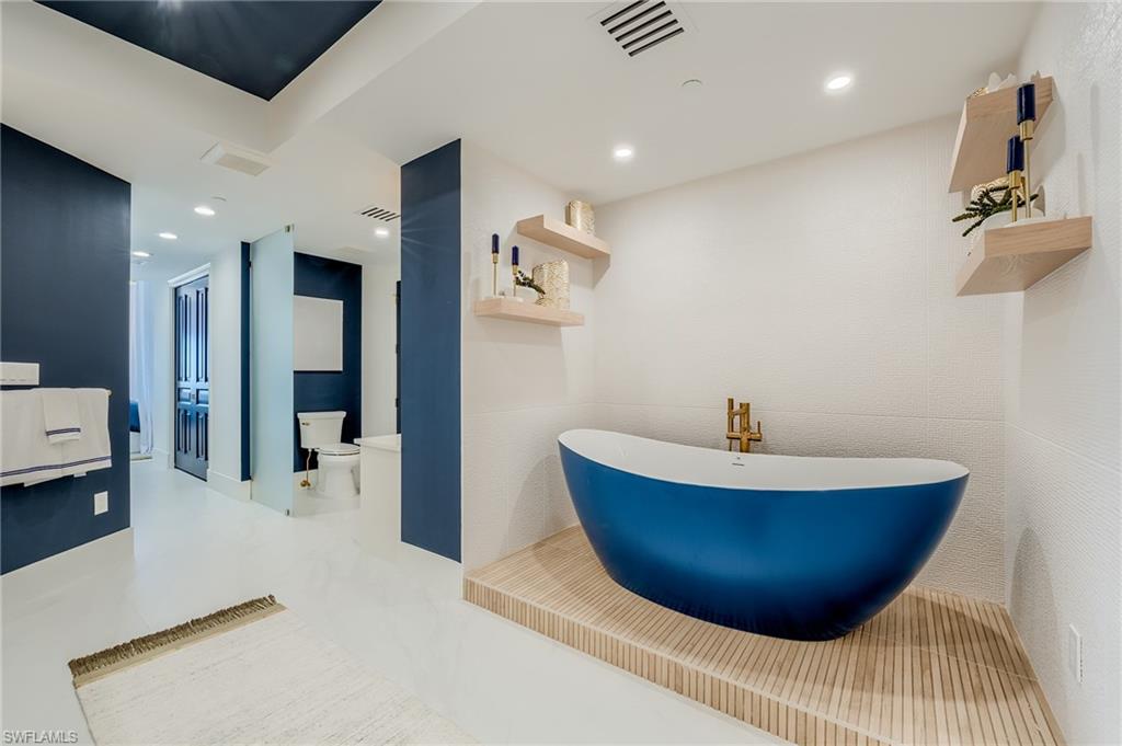 Contemporary bathroom with a blue freestanding tub on a raised wood-slat platform and navy accent walls.
