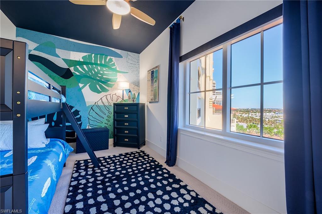 Bedroom with a blue bunk bed, tropical mural, and large windows overlooking the area.