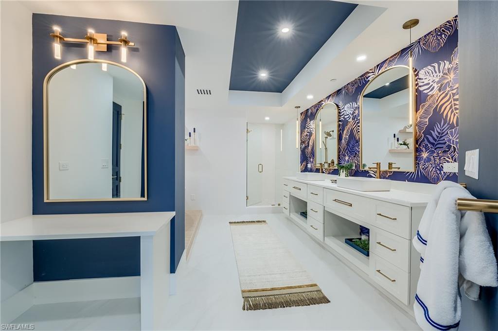 Bathroom with double vanity, arched mirrors, blue botanical wallpaper, and a glass-enclosed shower.