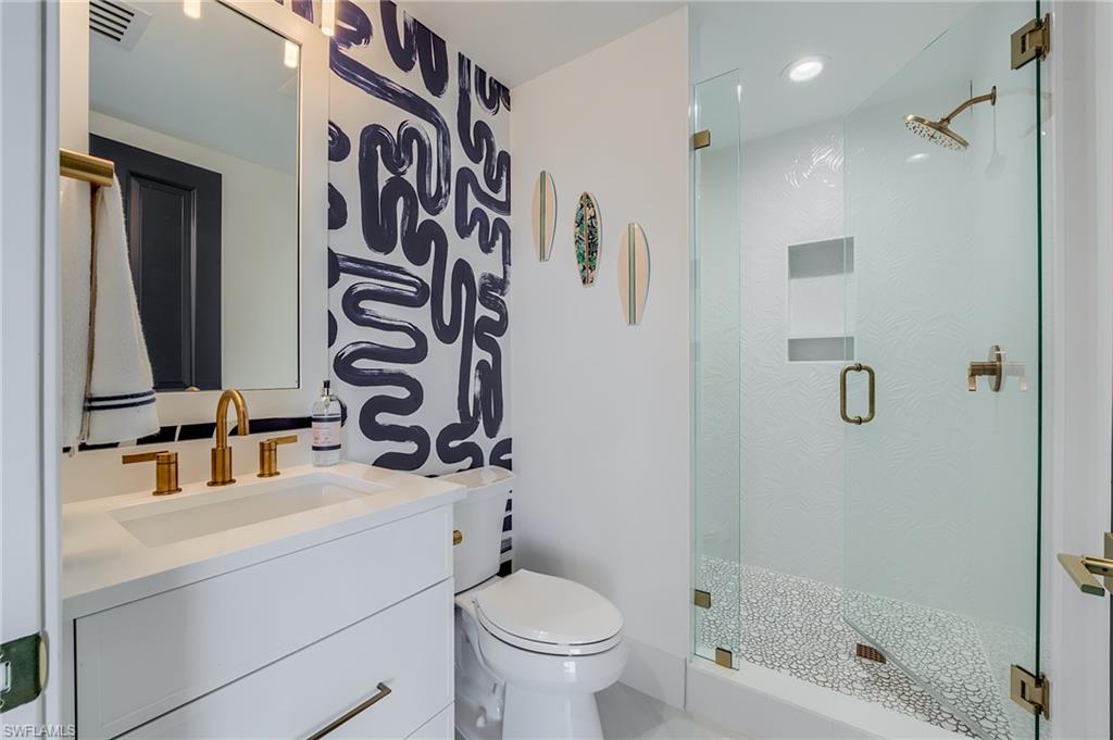 Modern bathroom with a patterned accent wall, white vanity, brass fixtures, and glass shower.