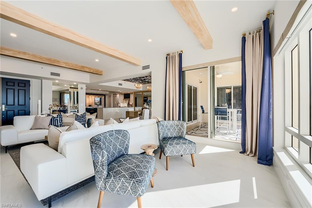 Furnished living room with white sofas, patterned blue chairs, wood ceiling beams, and sliding doors to a lanai.
