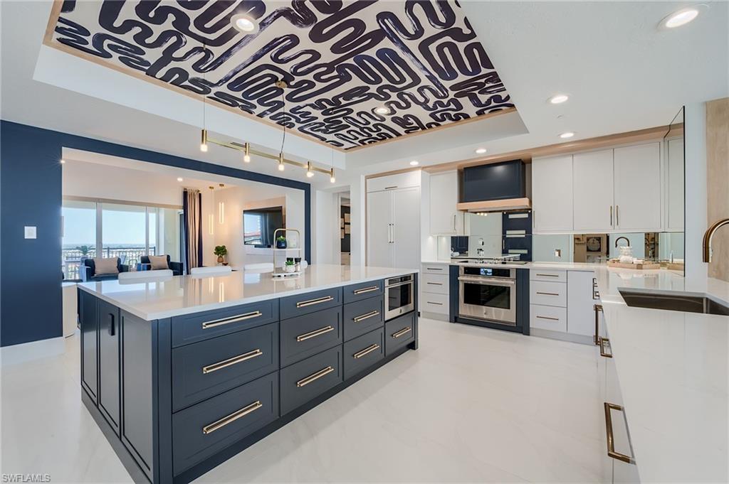 Modern kitchen with a navy island, white cabinetry, stainless steel appliances, and a patterned ceiling.