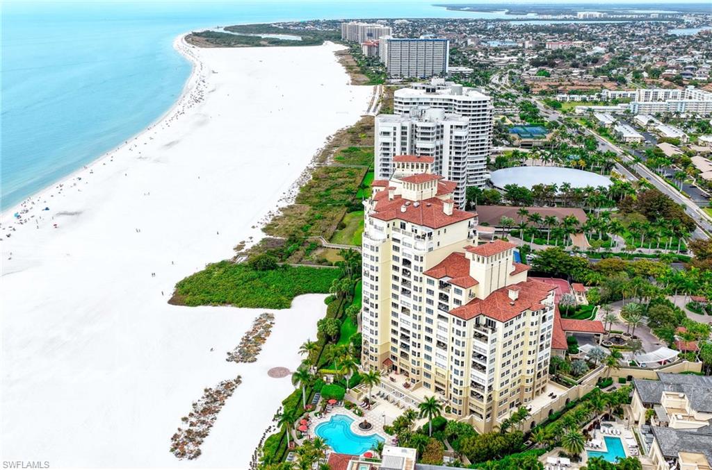 Beachfront condominium towers beside Marco Island’s white-sand beach, with the Gulf and resort pools visible.