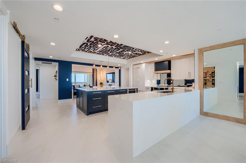 Contemporary condo kitchen with a large white island, navy cabinetry, and a patterned ceiling panel.