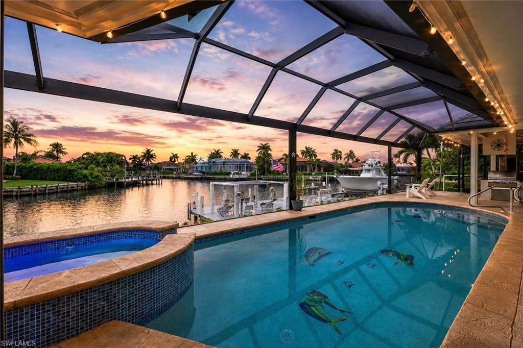Screened pool and raised spa overlook a canal and docked boat at sunset.
