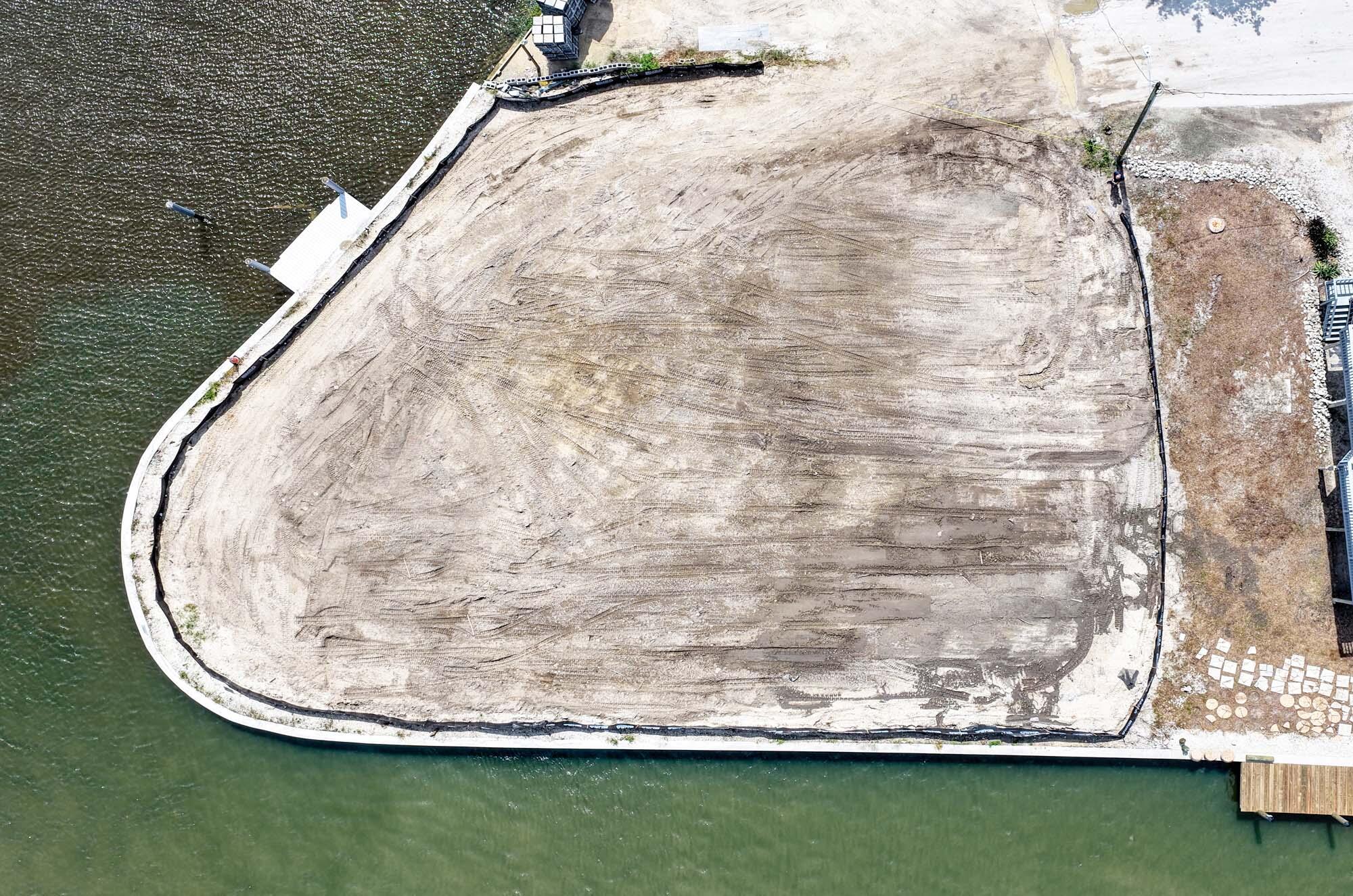 Graded waterfront lot with a curved seawall, dock, and water on two sides.