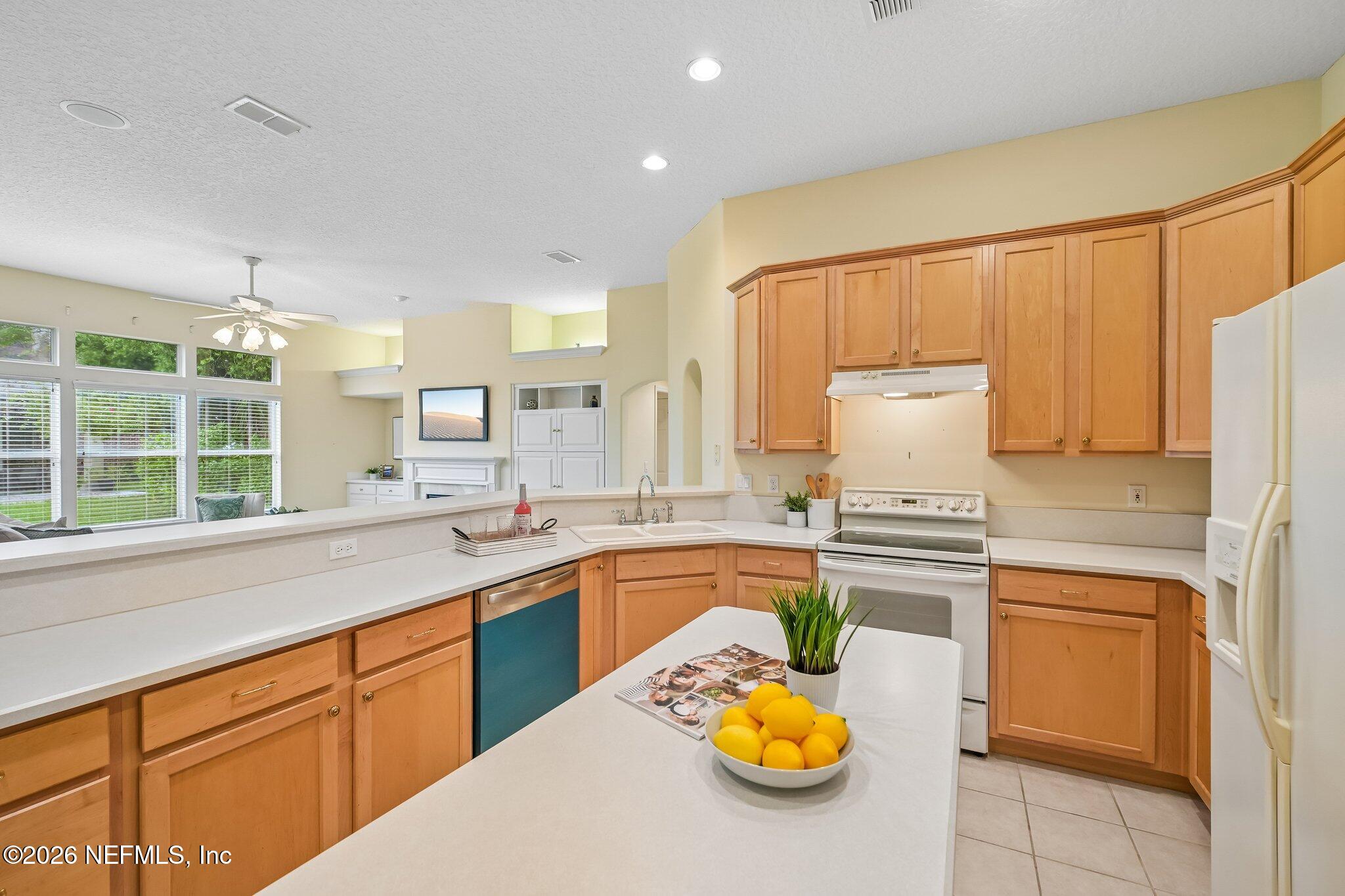 Kitchen with honey-colored cabinets, a large white island, and windows overlooking greenery.
