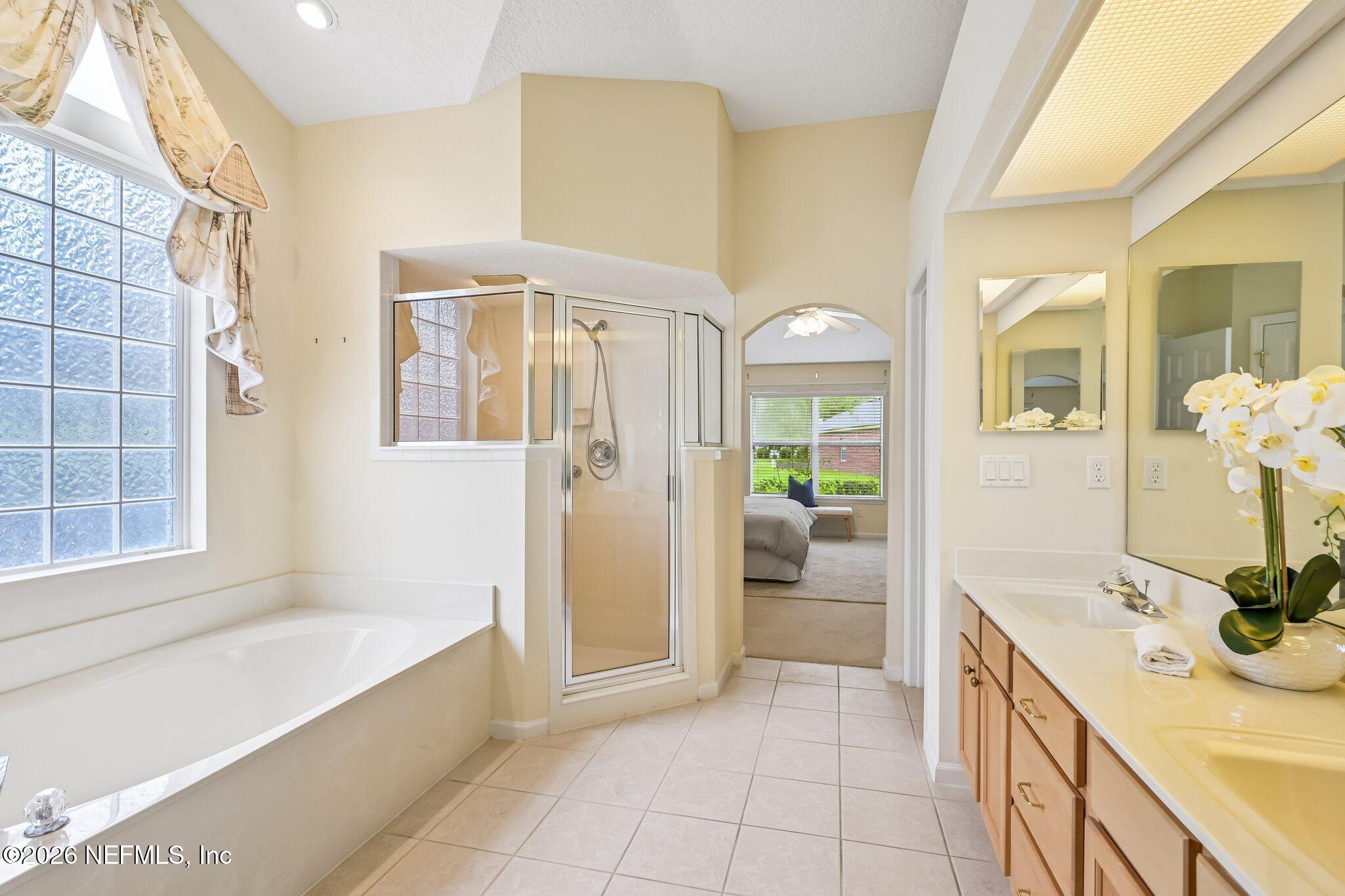 Primary bathroom with a soaking tub, glass shower, long vanity, and arched opening to the bedroom.