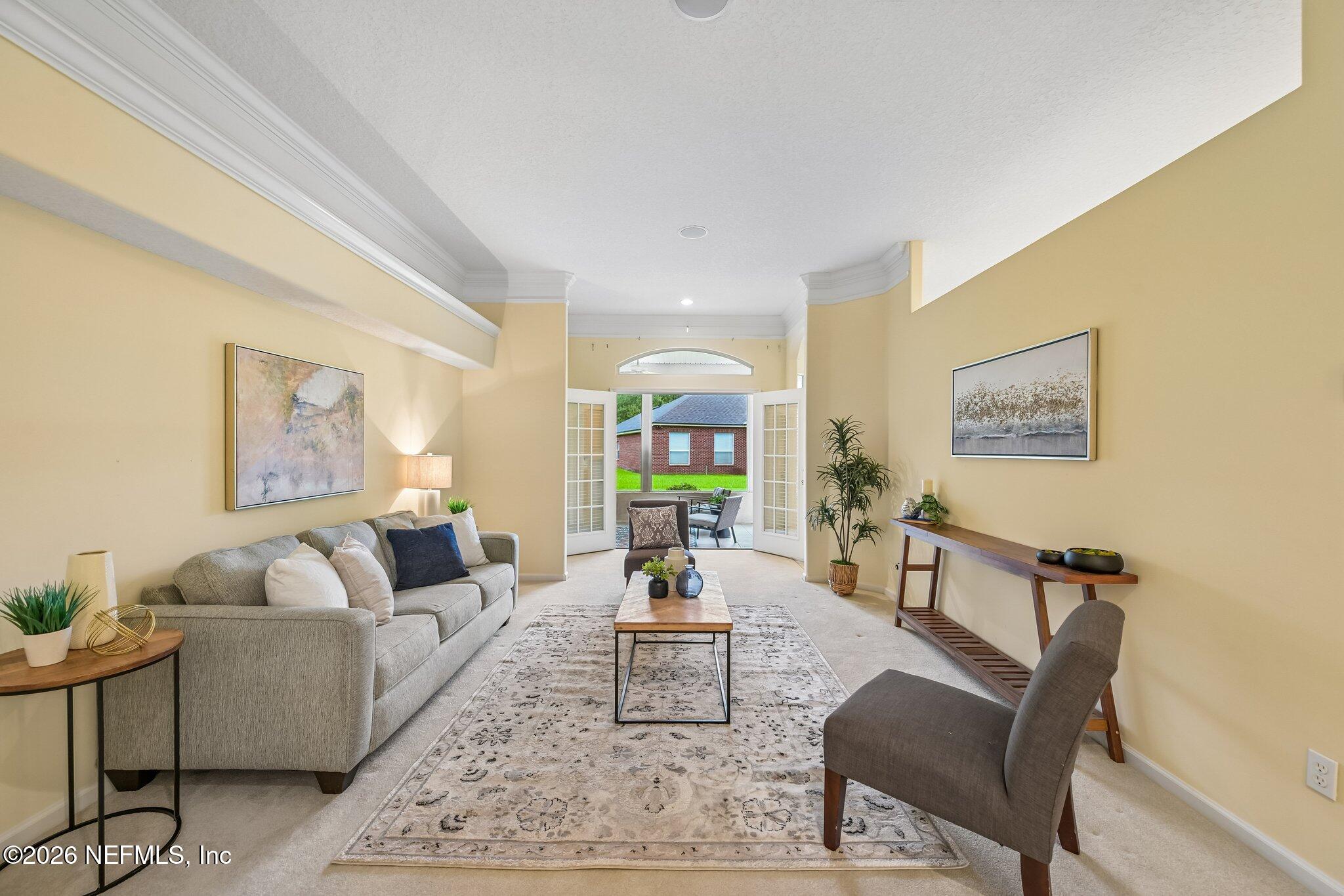 Staged living room with gray sofa and patterned rug, opening through French doors to a patio.