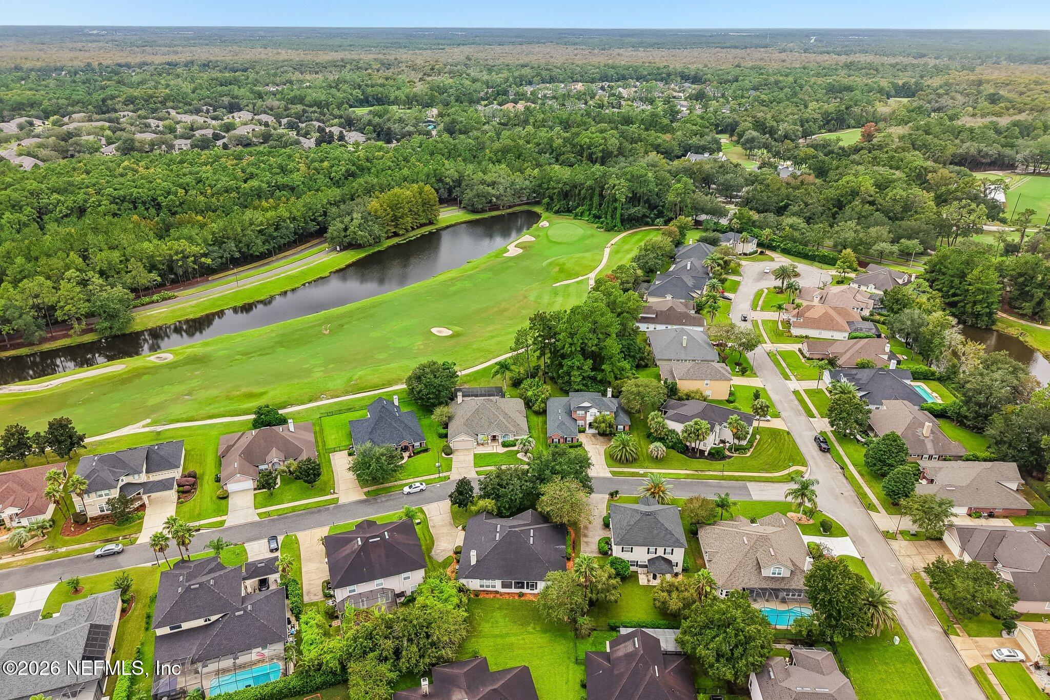 Aerial view of homes beside a golf course and pond, with sand bunkers and wooded surroundings.