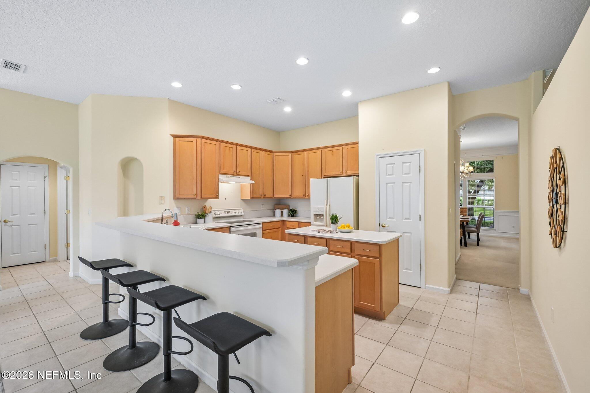 Kitchen with warm wood cabinets, a white breakfast bar, and black stools.