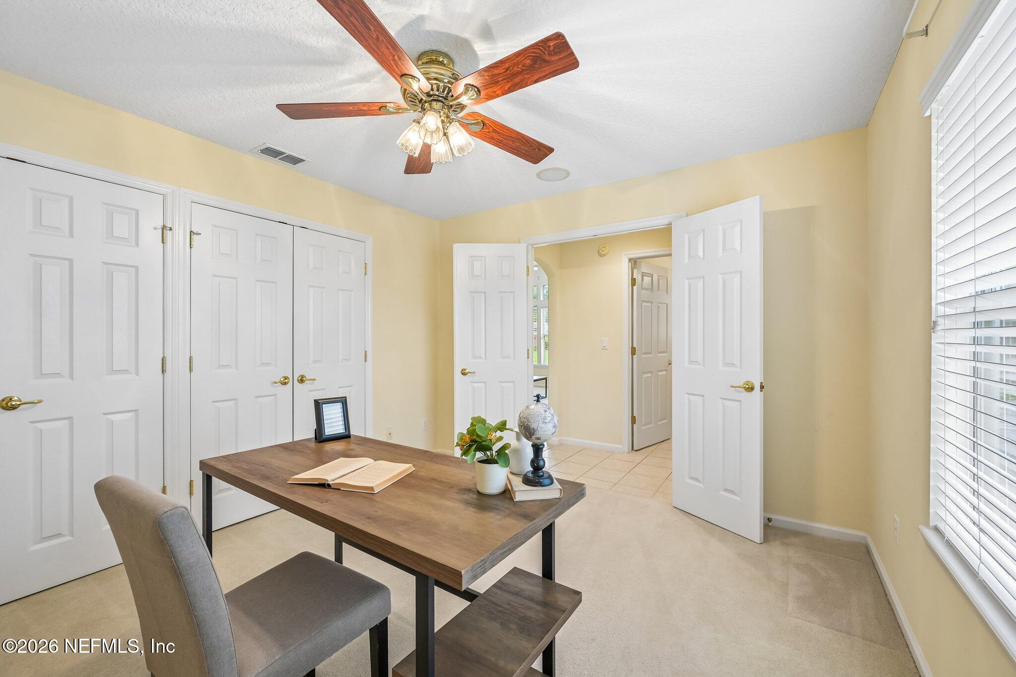 Furnished home office with a wood desk, gray chair, ceiling fan, and large closet doors.