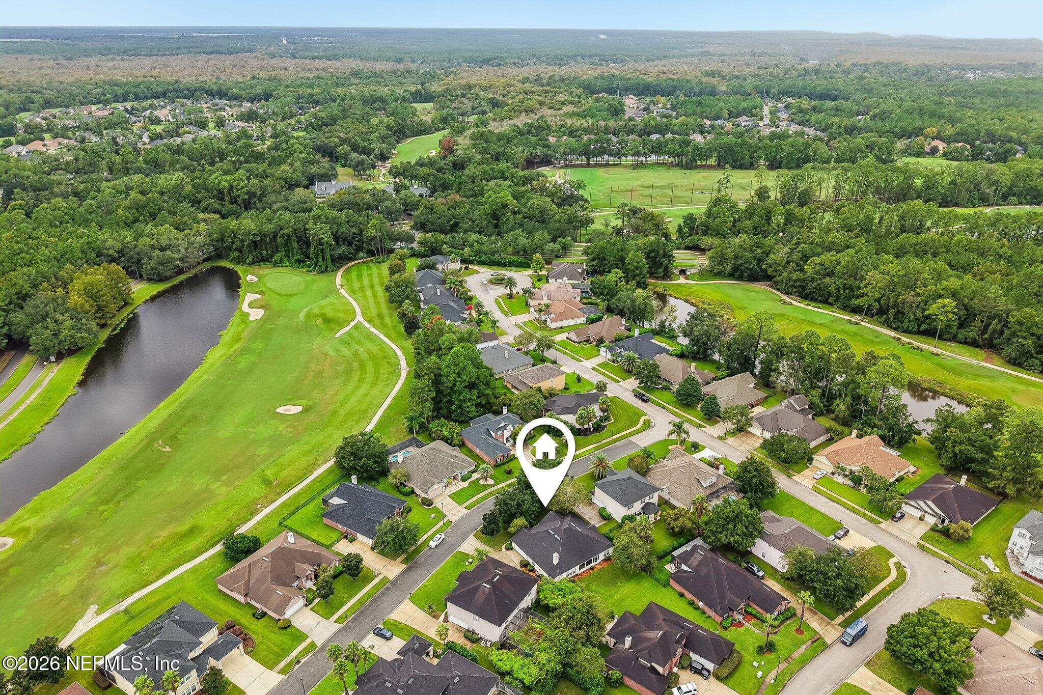Aerial neighborhood view with a golf course, pond, wooded surroundings, and marker identifying the home.