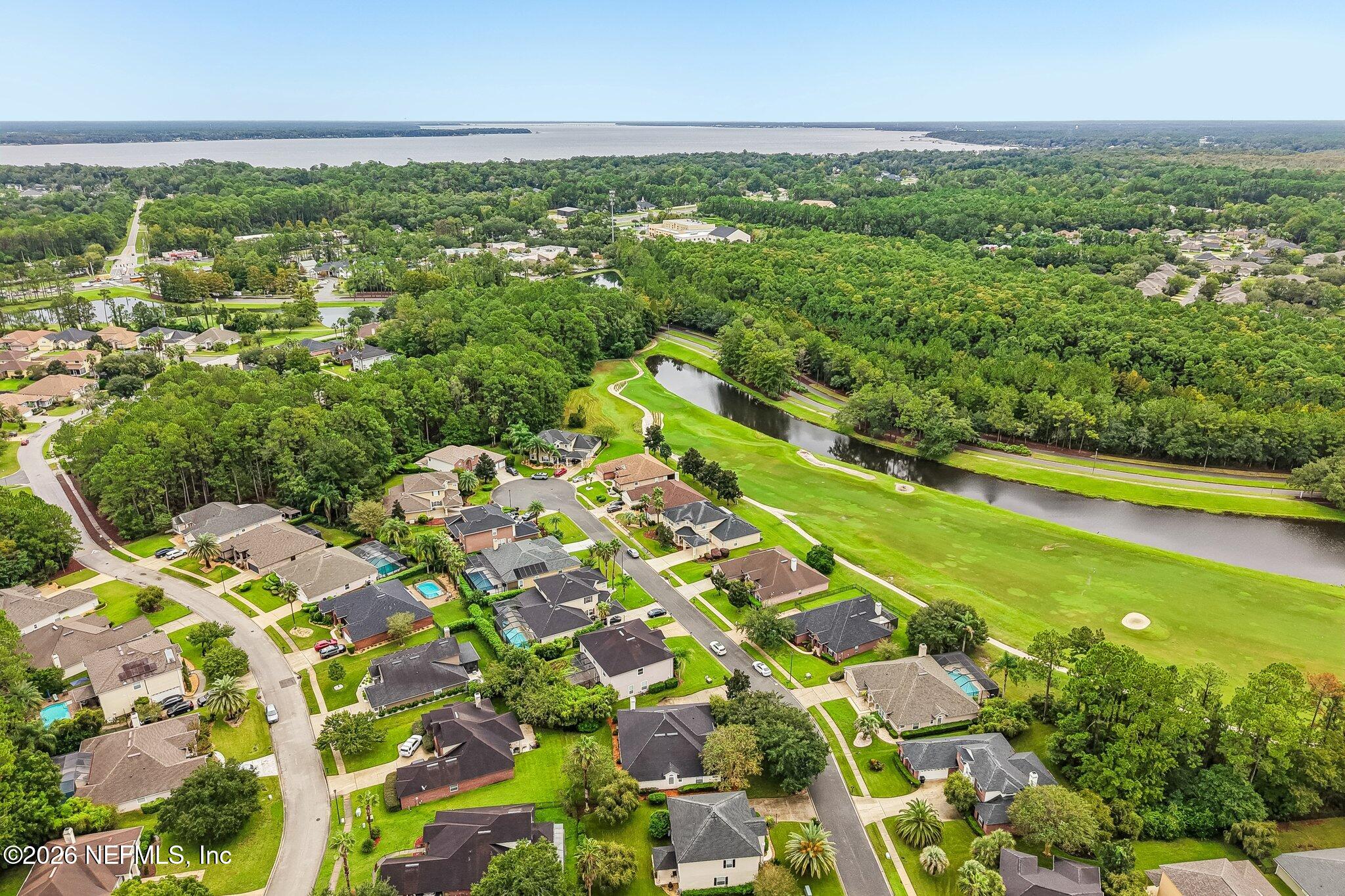Aerial view of homes beside a golf course, with a winding water hazard and wooded surroundings.