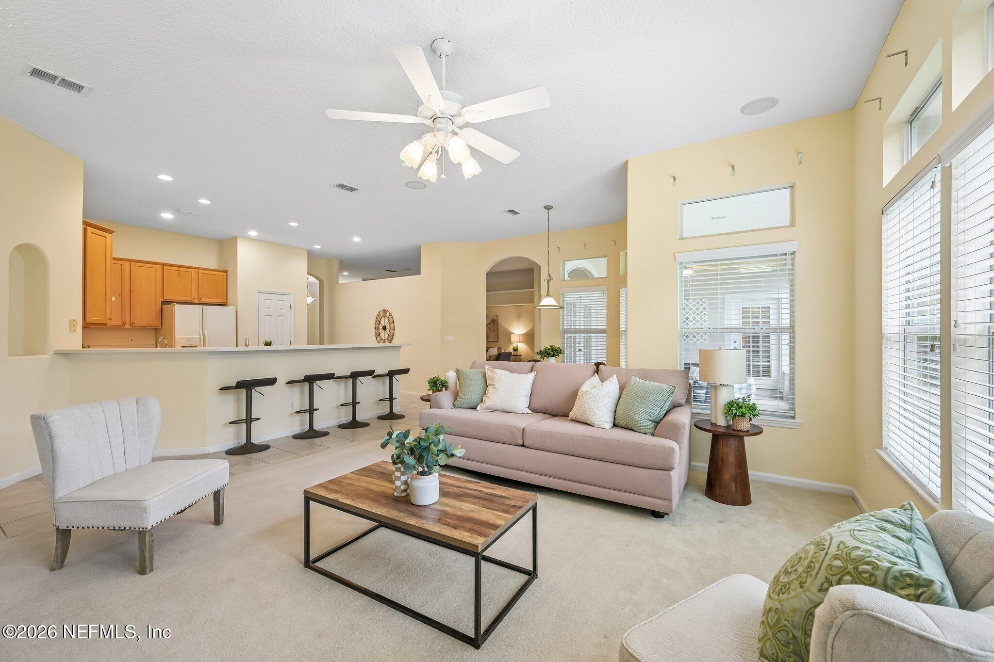 Open-plan living room and kitchen with a sofa, breakfast bar, and tall windows.