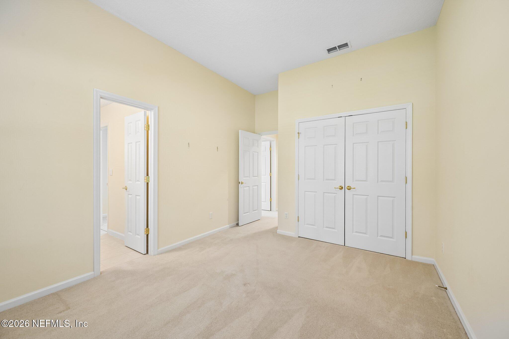 Empty carpeted room with pale yellow walls and white double closet doors.