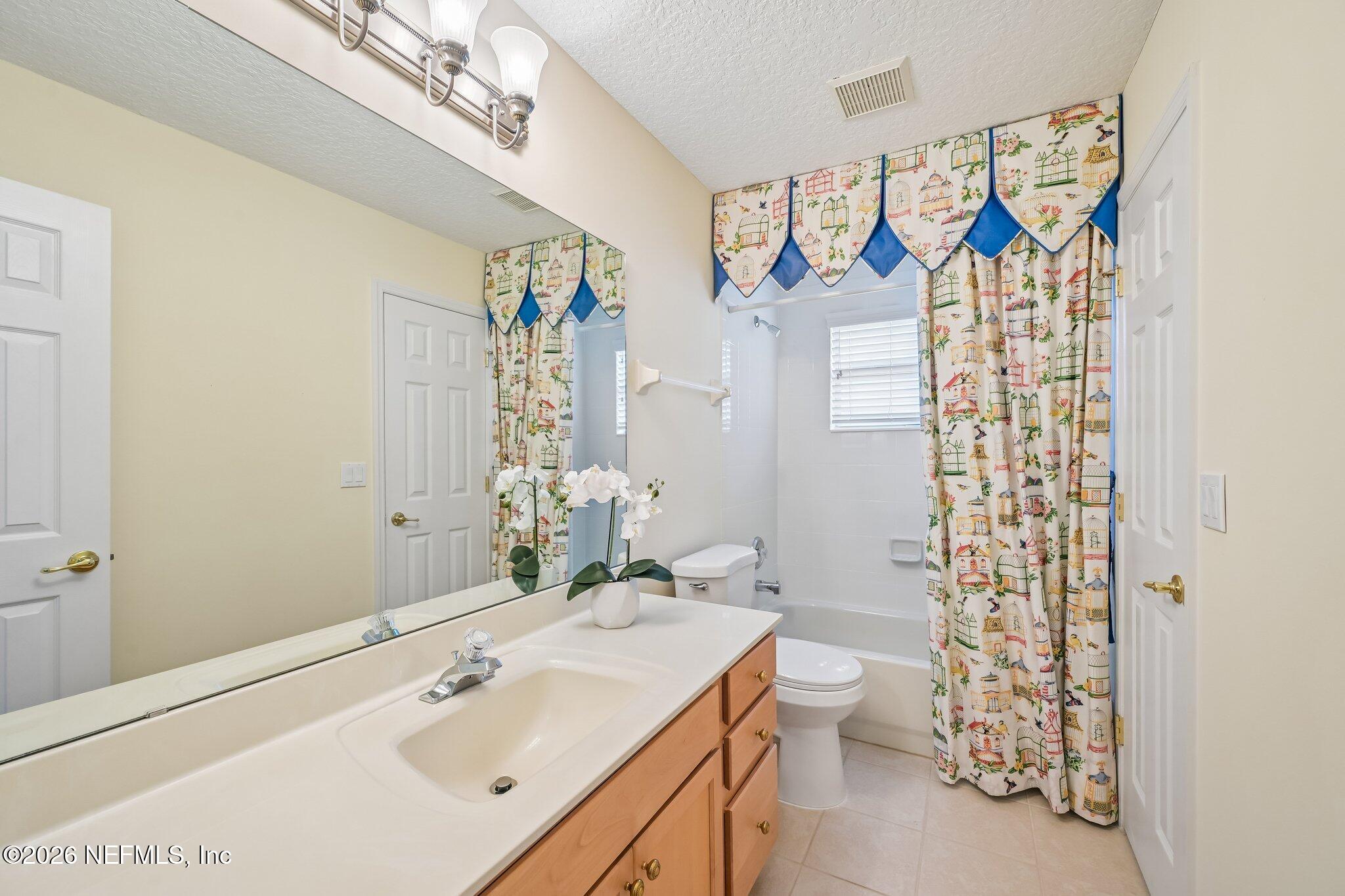 Bathroom with a long wood vanity, large mirror, and patterned curtains around the bathtub.