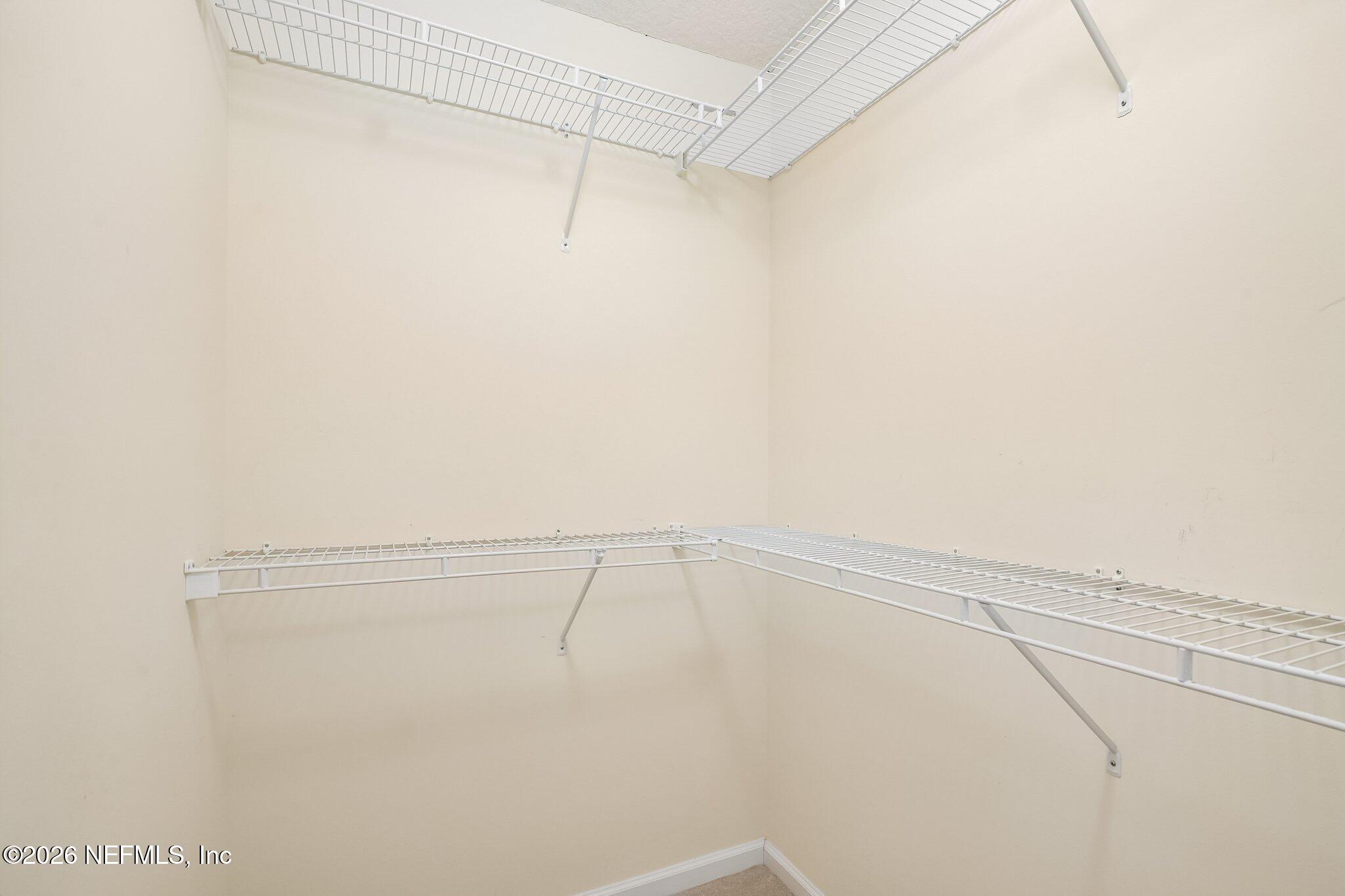 Empty walk-in closet with white wire shelving along the walls at two levels.