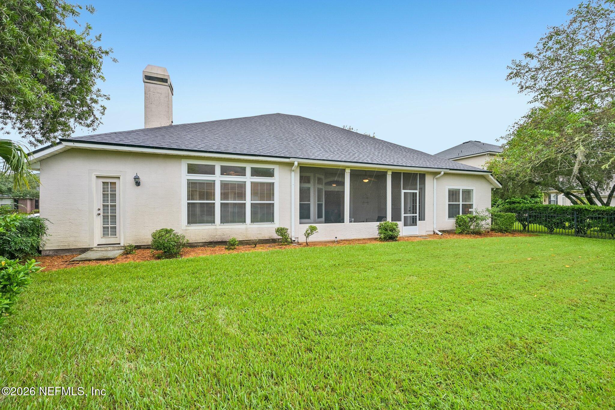 Rear of a light brick home with a screened porch and broad green lawn.