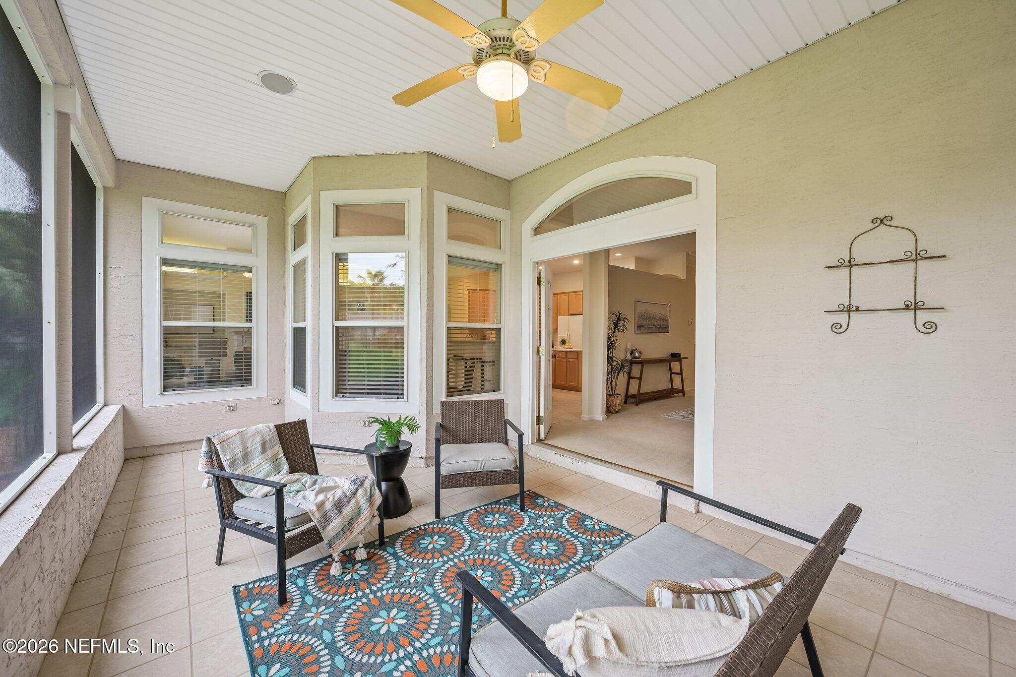 Enclosed patio with wicker seating, a colorful patterned rug, and an arched opening into the home.