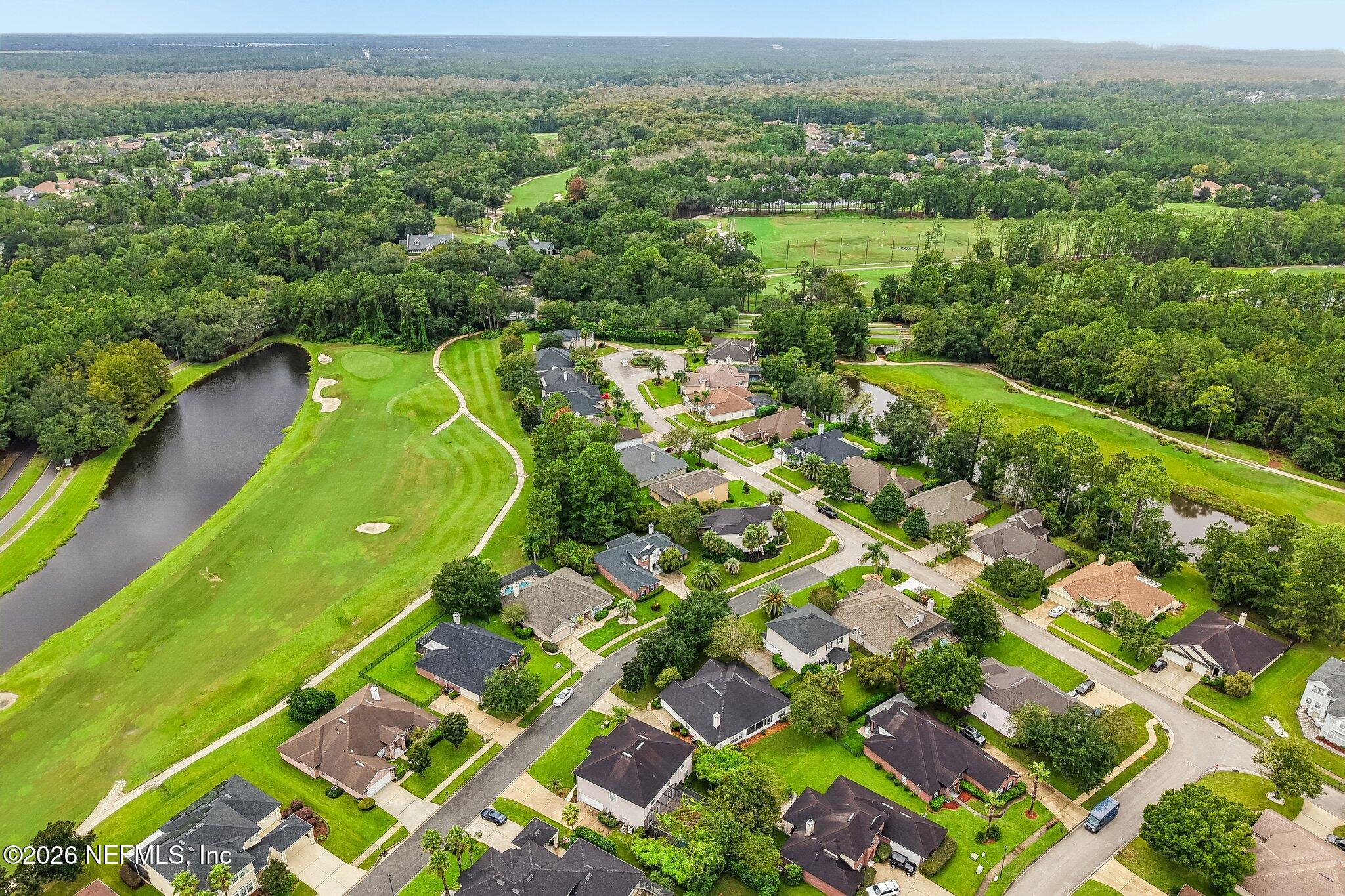 Aerial neighborhood view with homes beside a golf course and ponds.