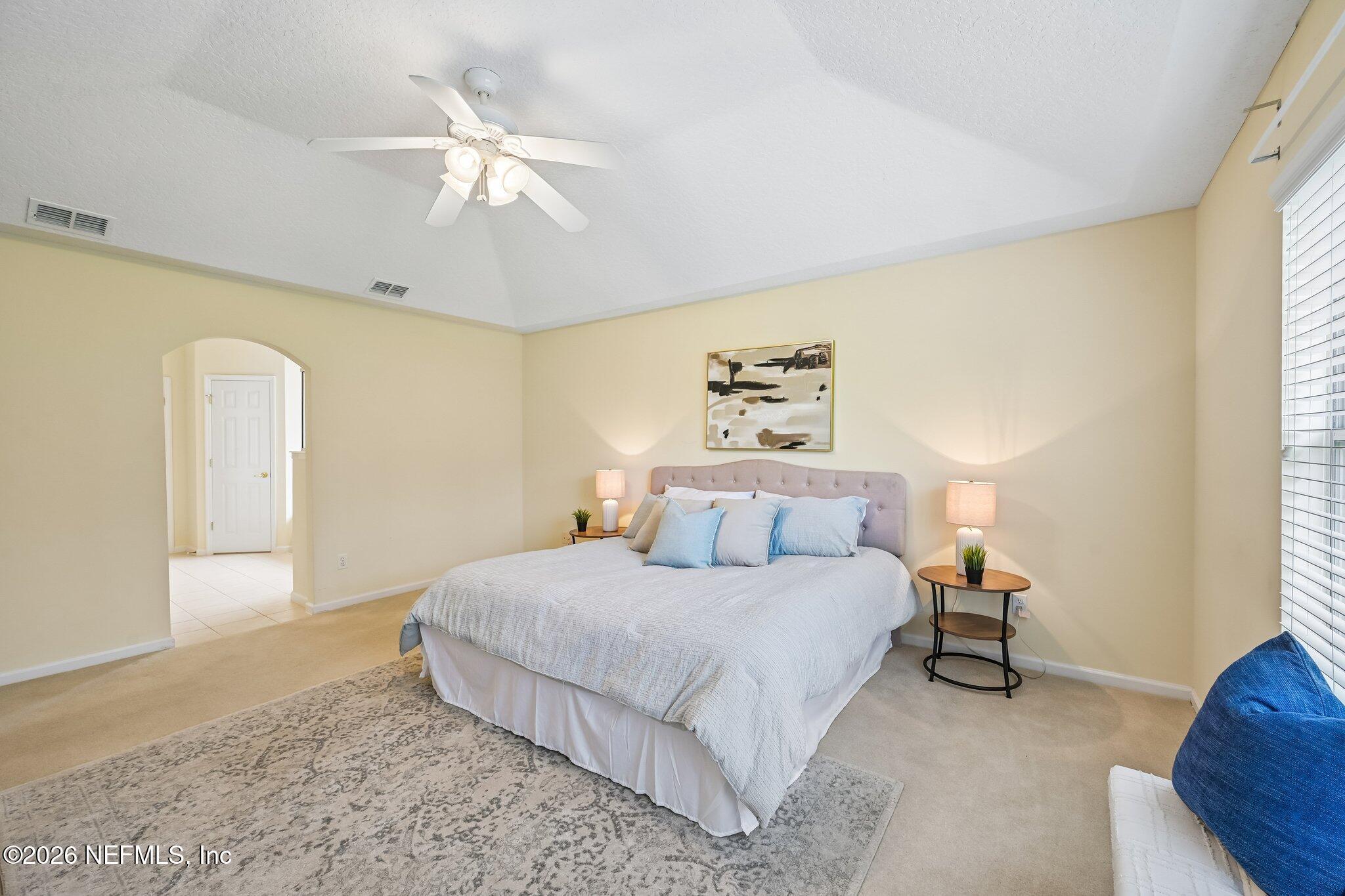 Staged bedroom with a large white-and-blue bed, tufted headboard, and ceiling fan.