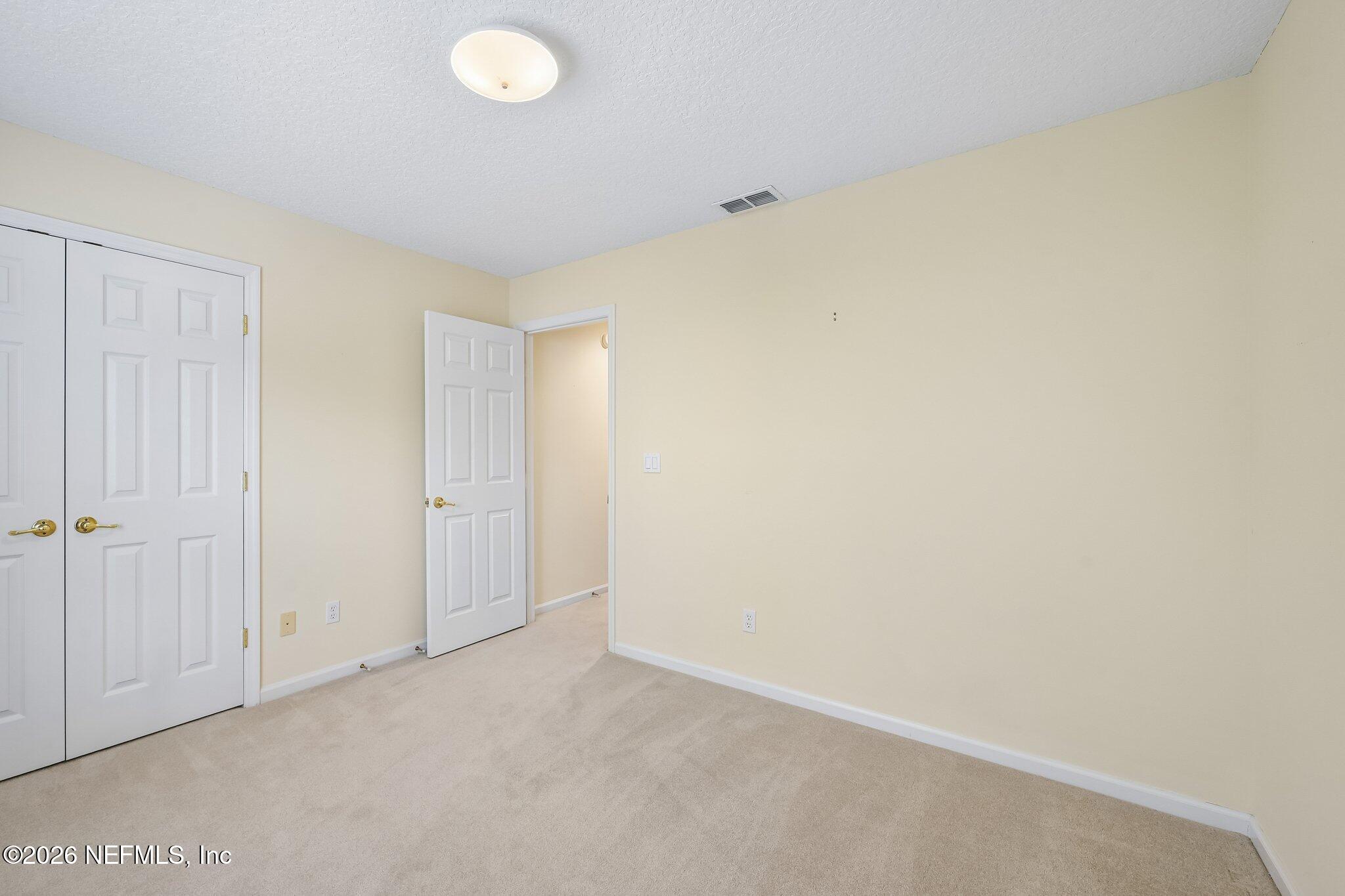 Empty carpeted room with white double closet doors and an open doorway.