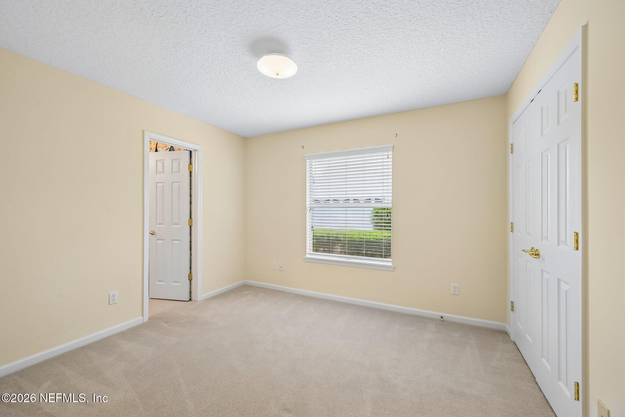 Empty bedroom with beige walls, light carpet, and a window with white blinds.