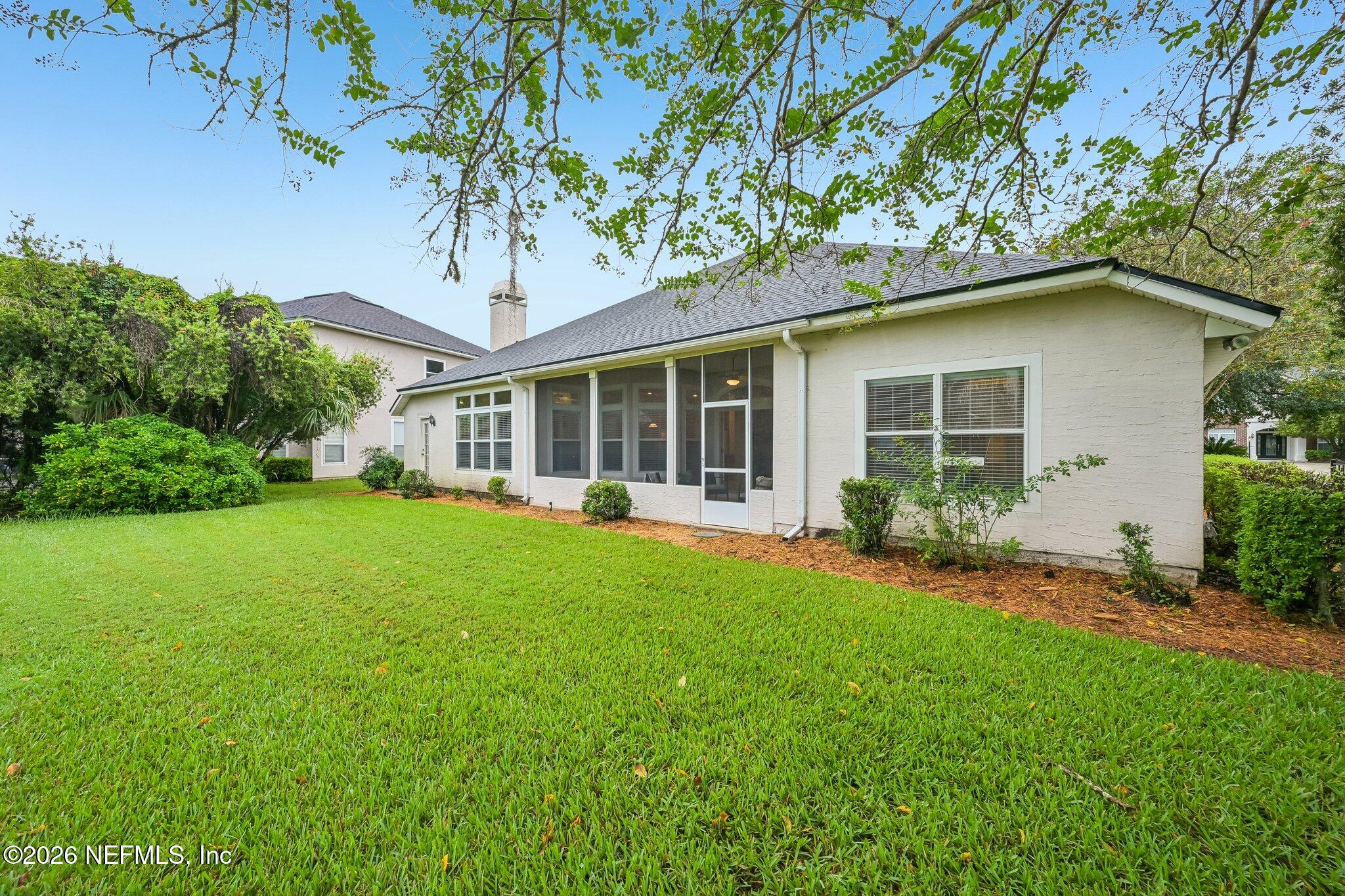 Rear of a light-colored home with a screened porch overlooking a broad green lawn.