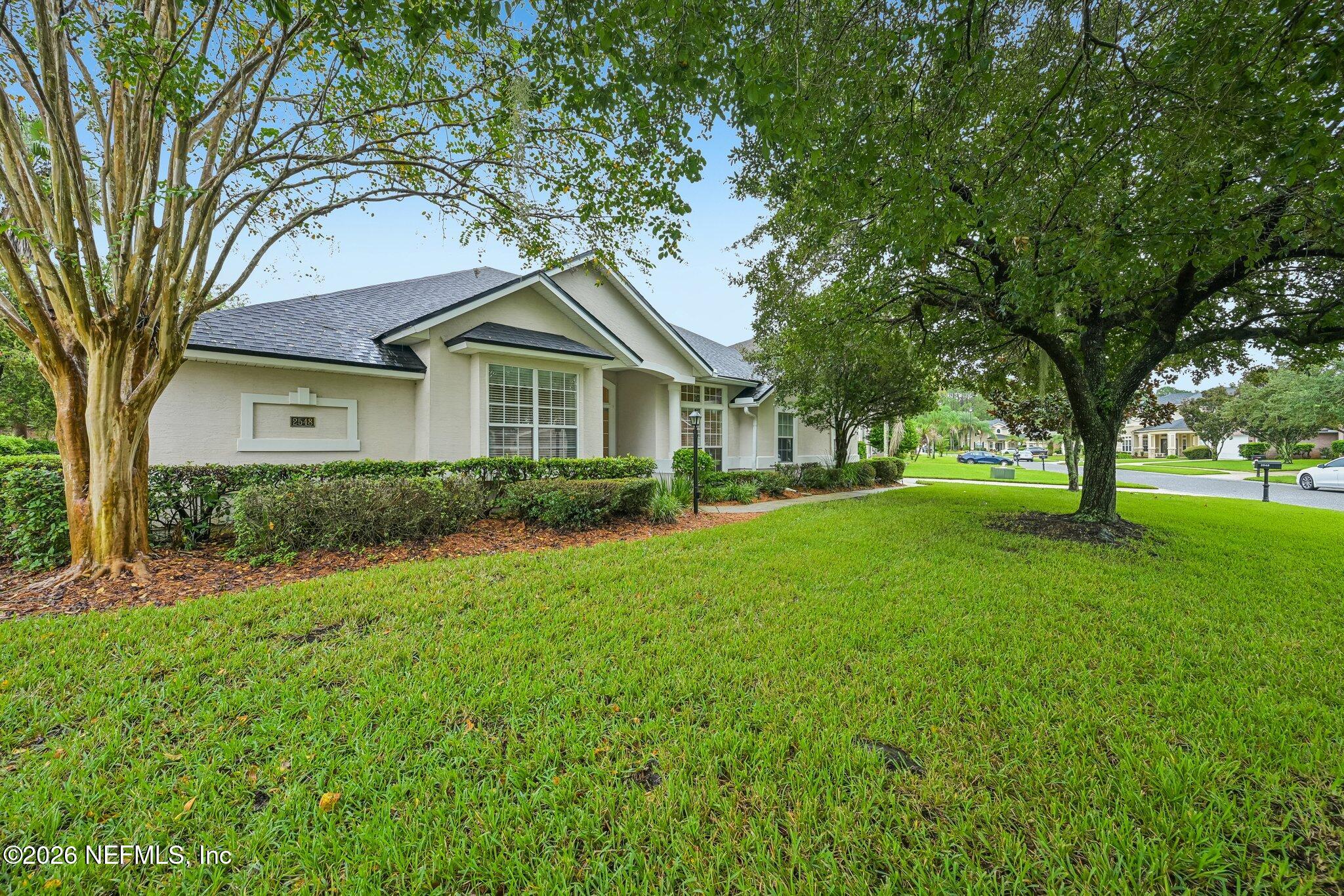 Single-story home with a dark roof, framed by mature trees above a broad front lawn.
